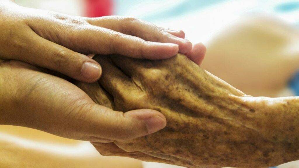 Nuori hoitaja pitelee vanhuksen kättä omissaan