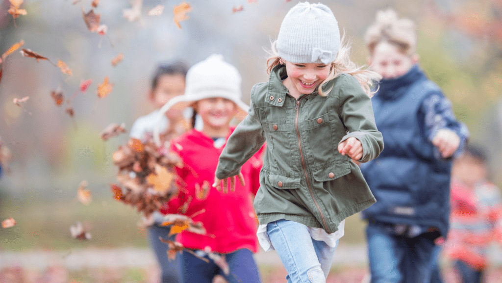 Lapset juoksevat syksyllä lehtisateessa